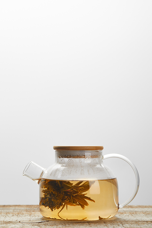 glass teapot with chinese blooming tea on wooden table isolated on grey with copy space