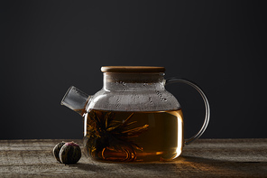 transparent teapot with blooming tea and tea balls on wooden table isolated on black