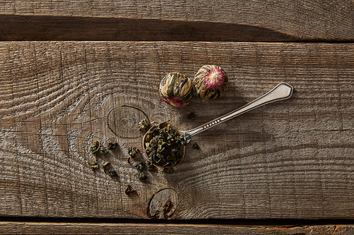 top view of spoon with green tea and blooming tea balls on wooden table