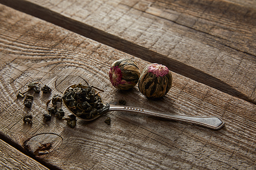 spoon with green tea and blooming tea balls on wooden table
