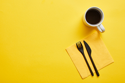 Top view of cup of hot delicious coffee and disposable fork and knife with yellow napkin on yellow background