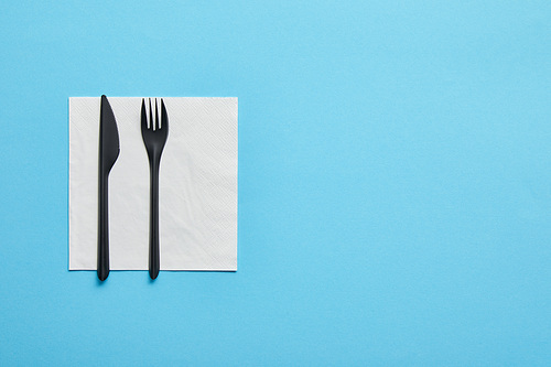 Top view of disposable fork and knife lying on napkin on blue background