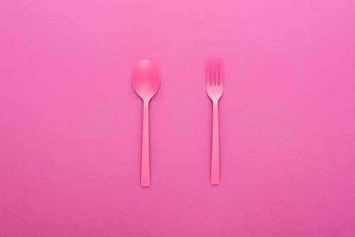 pink plastic spoon and fork isolated on pink