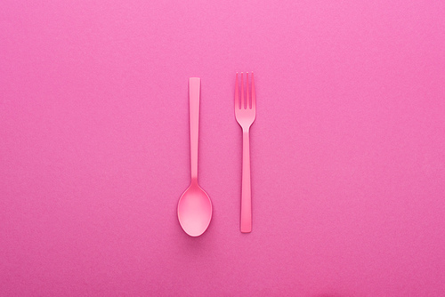 pink plastic spoon upside down and fork on pink background