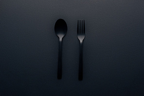 top view of plastic spoon and fork on black background