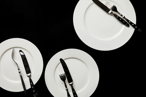 top view of white round plates with cutlery isolated on black