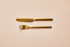 top view of golden fork and knife on pink background