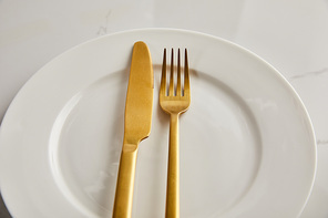 golden knife and fork on clean white plate on marble table