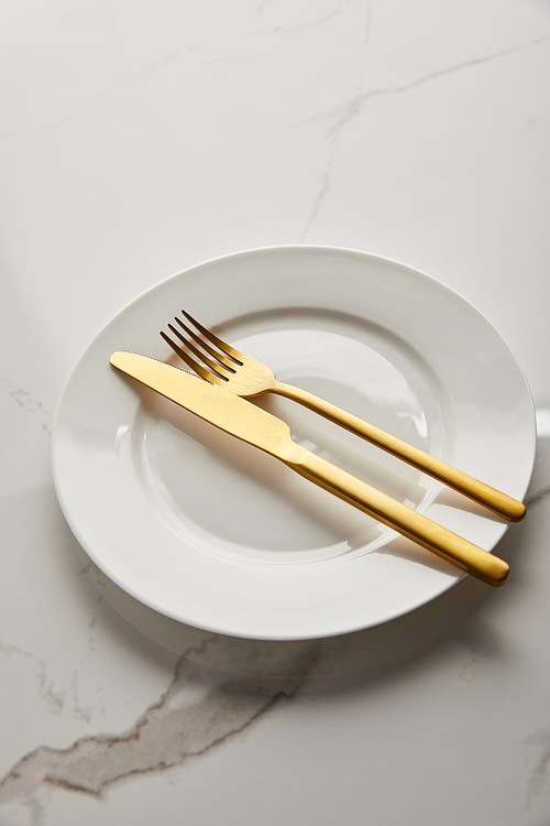 clean white plate with shiny golden knife and fork on marble table