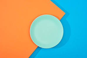 top view of empty plate on colorful blue and orange surface