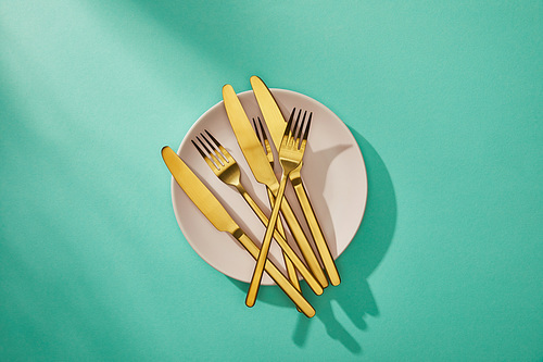 Top view of golden forks and knives on plate on turquoise background