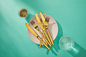 Top view of golden cutlery on plate with coffee and water in glasses on turquoise surface