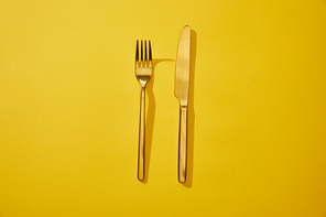 Top view of shiny fork and knife on yellow background with copy space