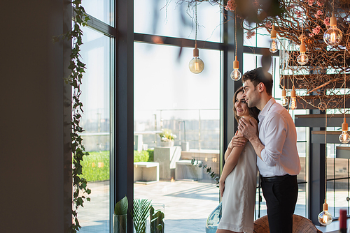 man in shirt hugging smiling woman in slip dress in restaurant