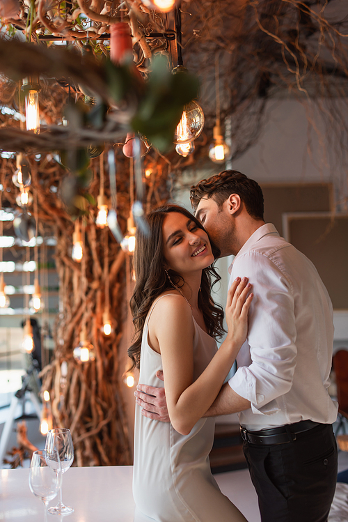 man kissing cheerful young woman in restaurant
