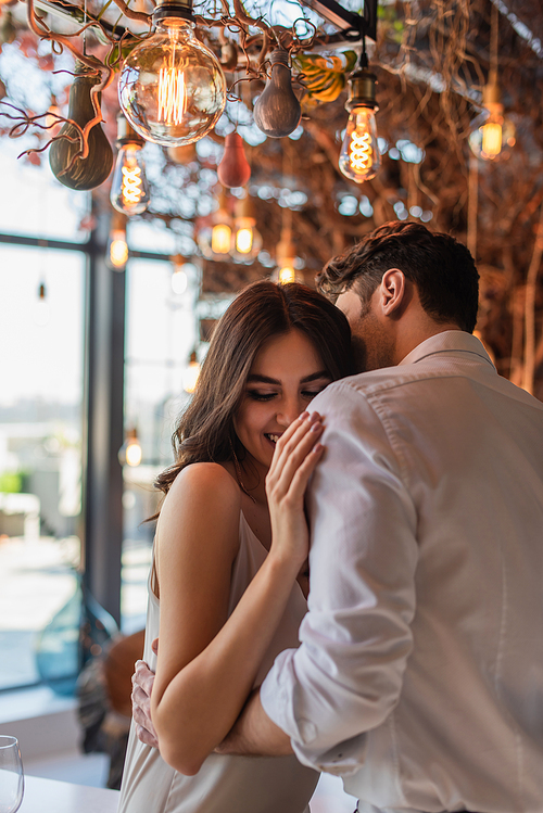 man kissing and hugging cheerful young woman in restaurant