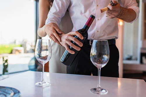 cropped view of woman hugging boyfriend opening bottle of red wine in restaurant