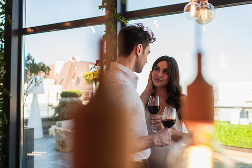 cheerful woman holding glass of wine and looking at man in restaurant