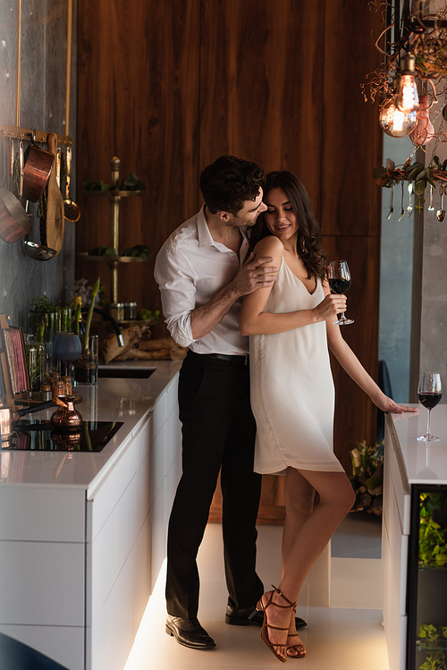 man seducing smiling girlfriend in slip dress with glass of wine