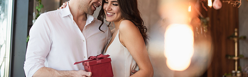 happy man holding red gift box near smiling girlfriend in slip dress, banner