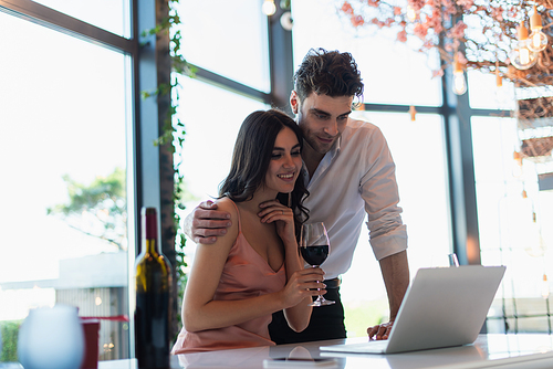 happy couple watching movie on laptop near bottle of wine