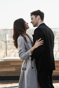 cheerful man and happy woman looking at each other while embracing on terrace of restaurant