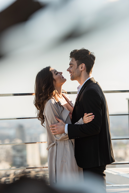 side view of smiling man and happy woman looking at each other while embracing on terrace of restaurant