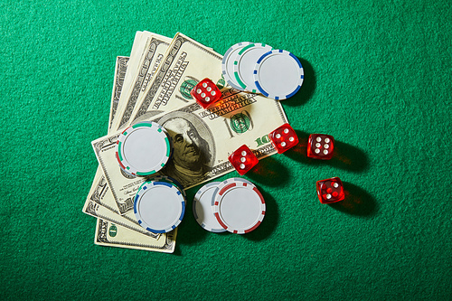 Top view of dollar banknotes, dice and casino chips on green