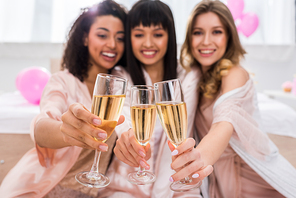 selective focus of smiling multicultural girls clinking with glasses of champagne on bachelorette party