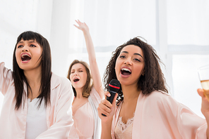 beautiful smiling multicultural girls singing with microphone on pajama party