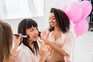 multiethnic girls making hair styling, makeup and drinking champagne on bachelorette party