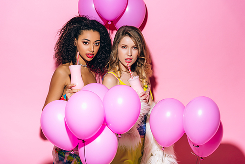 sexy multicultural girls drinking milkshakes on pink with balloons