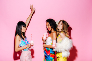 emotional stylish multiethnic girls drinking milkshakes on pink