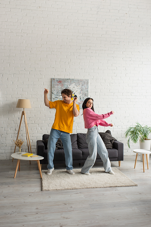 positive young couple in casual clothes dancing in living room