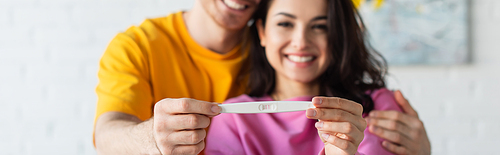pregnancy test in hands of blurred smiling young couple at home, banner