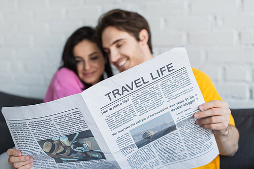 smiling young couple sitting on couch, hugging and holding newspaper at home