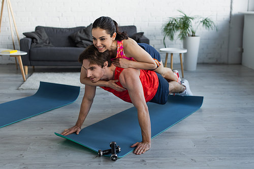 smiling fit young woman lying on back of man doing plank at home