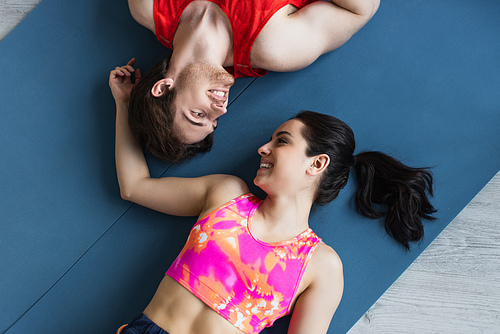 top view of smiling young couple in sportswear lying on fitness mats and looking at each other at home