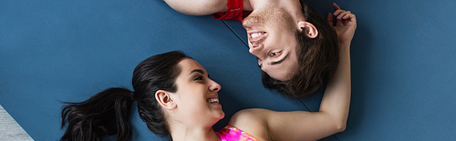 top view of young couple in sportswear lying on fitness mats and looking at each other at home, banner