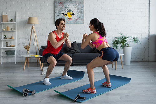 positive young couple in sportswear doing squats on fitness mats in modern loft