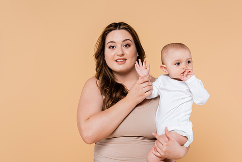 Smiling plus size parent holding hand of baby daughter isolated on beige