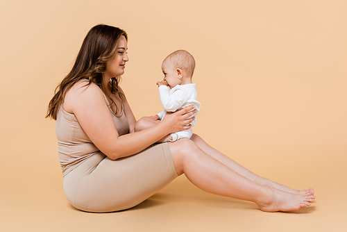 Young plus size woman holding kid while sitting on beige background
