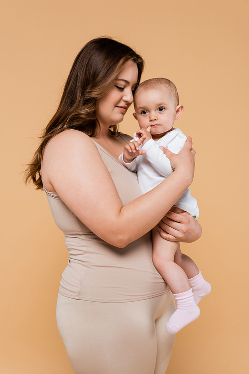 Young plus size woman hugging daughter isolated on beige