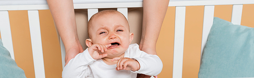 Plus size woman holding crying daughter in crib isolated on beige, banner