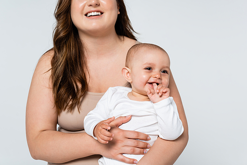 Cheerful plus size woman holding cheerful baby isolated on grey