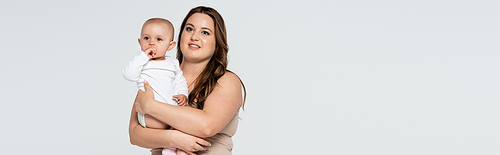 Smiling plus size woman holding baby daughter isolated on grey, banner