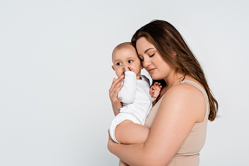 Pretty plus size mother hugging baby daughter isolated on grey