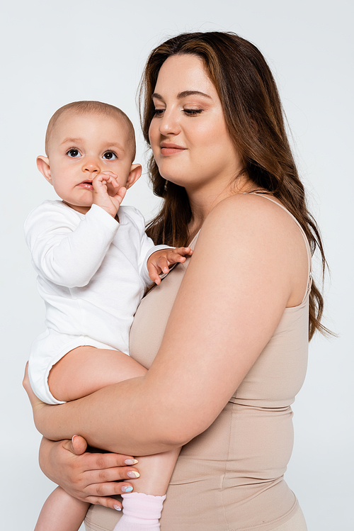 Smiling mother with overweight hugging baby girl isolated on grey