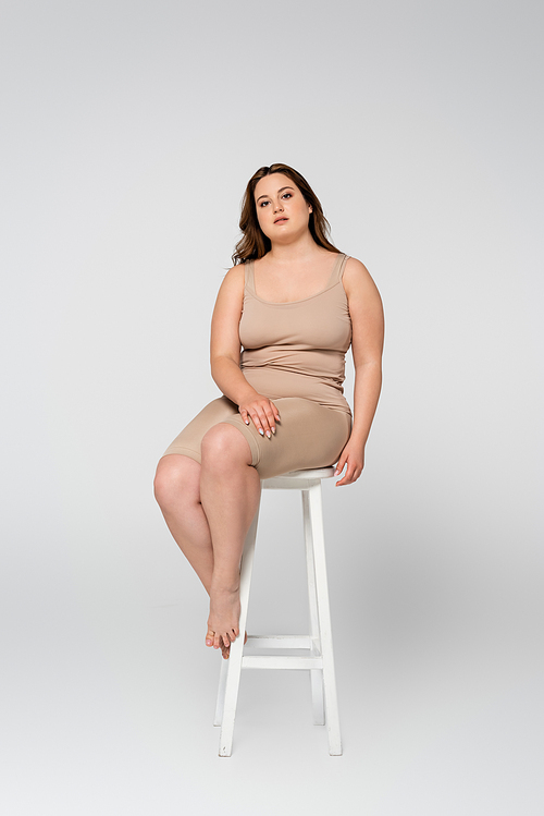 Pretty plus size woman  while sitting on chair on grey background