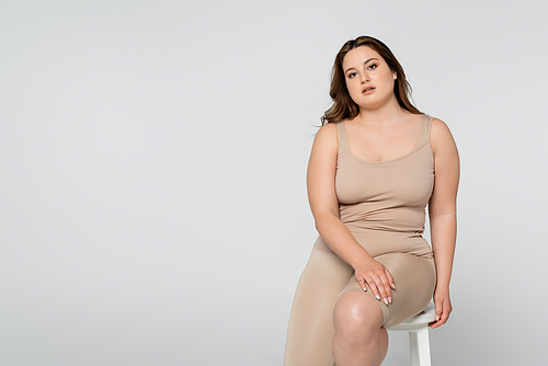Brunette body positive woman sitting on chair and  isolated on grey